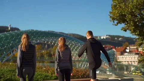 Group of friends doing step ups in the park with a bridge on the background Video stock 70967488