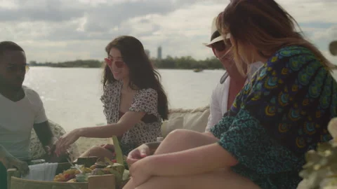 Group of friends eating and drinking and talking at a picnic on the beach in Aus Stock Footage 199459714
