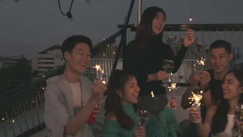 Group of friends enjoying drinks and lighting sparklers during rooftop party at Stock Footage 284416631