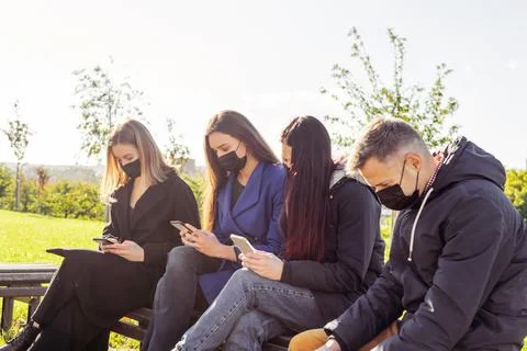 Group of friends with face masks using smartphones Stock Photos