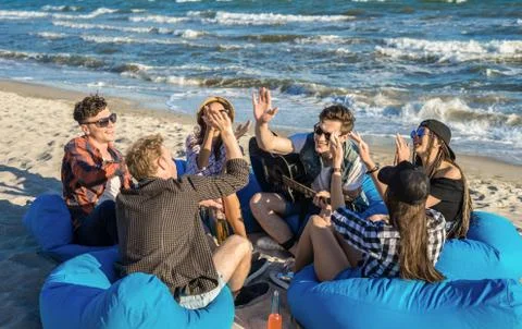 Group of friends giving high five on beach sitting on bean bags Stock Photos