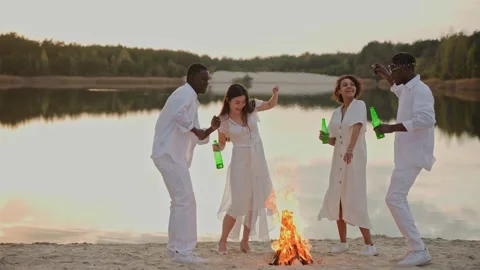 Group of friends having fun and dancing on a lake beach drinking near campfire Stock Footage 197169846