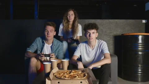 Group of friends having fun playing on game console in dark room. One man eats Stock Footage 136333185