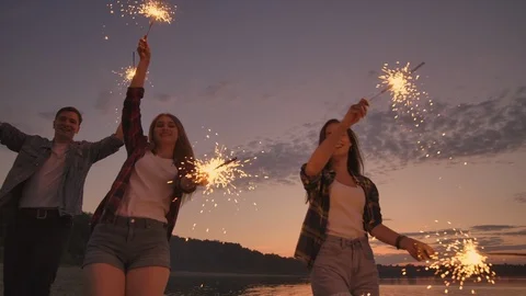 Group of friends having fun running on the beach with sparklers. Видео 116168582