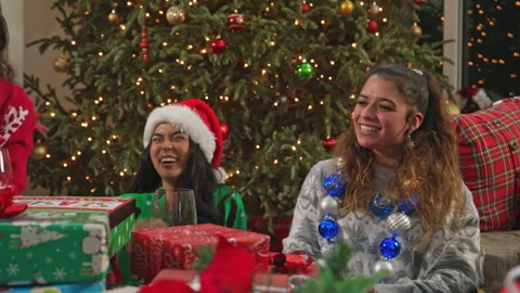 Group of friends laugh and exchange gifts beneath a decorated Christmas tree. Stock Footage 340928538