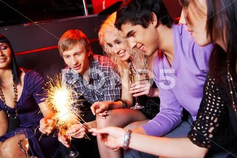 Group of friends looking at sparkling bengal lights during party Stock Photos