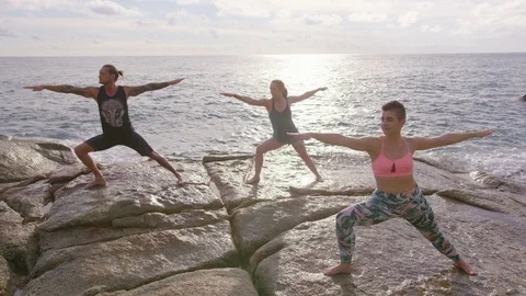 Group of friends practicing warrior pose on rock at seaside Stock Footage 74778629