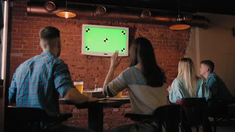 A group of friends in the pub looking at the green TV screen jump up from their Stock Footage 186238152