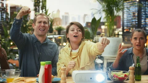 Group of friends react to projected sports match while sharing food and drinks Stock Footage 347067992