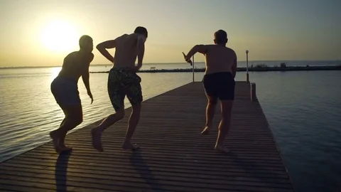 Group of friends running and jumping off sea pier in the water rapid slow motion Stock Footage