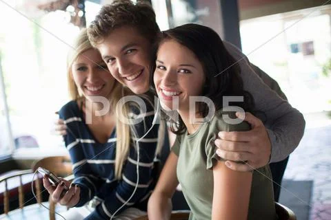 Group Of Friends Sharing Earphones In Coffee House