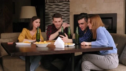A group of friends sit in a bar with beer and pizza, they look at the phone. Stock Footage 146301016