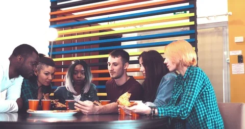 Group of friends sit at a table, eat pizza and look at the phone to their friend Stock Footage 88688700