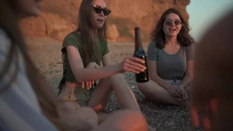 Group of the friends is sitting on the beach, drinking beer and clinking bottles Stock Footage 135256973