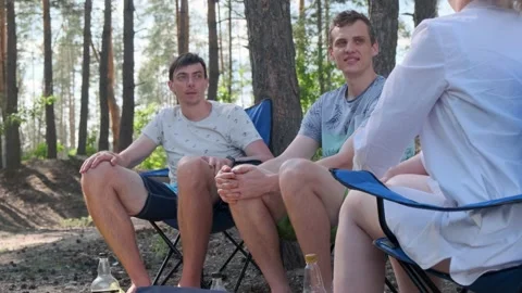 Group of friends sitting on chairs in a pine forest and talking Stock-Footage 135672576
