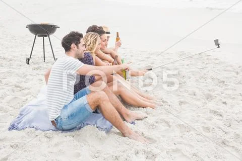 Group of friends sitting on the sand taking selfie with selfie stick Stock Photos