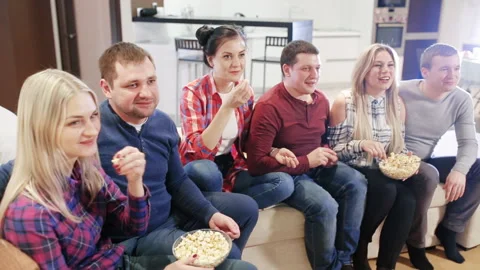Group of friends sitting on the sofa, watching TV and laughing Stock Footage 87160961