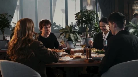 Group of friends sitting at table with delicious food and drinks in restaurant Stock Footage 315230959