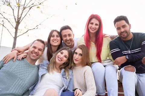 Group of friends smiling at the camera while sitting together on a bench. 스톡 사진