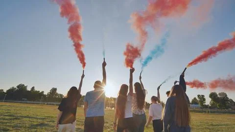 A group of friends spraying multi-colored smoke at sunset. Stock Photos