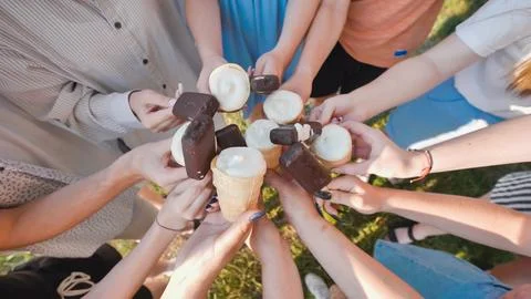 Group of friends is standing together on a patch of grass, holding ice cream Stock Photos