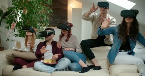 Group of friends using virtual reality simulator glasses in living room. Shot in Stock Footage 118065947