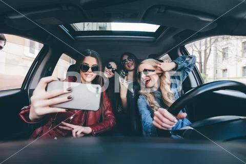 Group of girls having fun in the car and taking selfies with camera on road.. Stock Photos