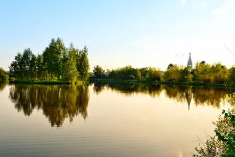 A group of green trees is reflected in the mirror surface of the lake. Stock Photos