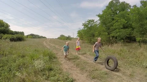 Group of happy children running down the hill in a meadow and roll the wheel. Stock Footage 53307799