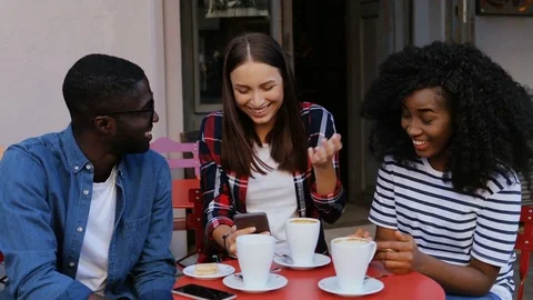 Group of happy multi-ethnic friends sitting at table in cafe, laughing and Stock Footage 81836500