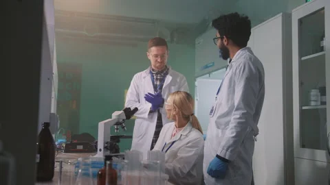 Group of happy scientists with glasses looking under a microscope in a light Stock Footage 243904410