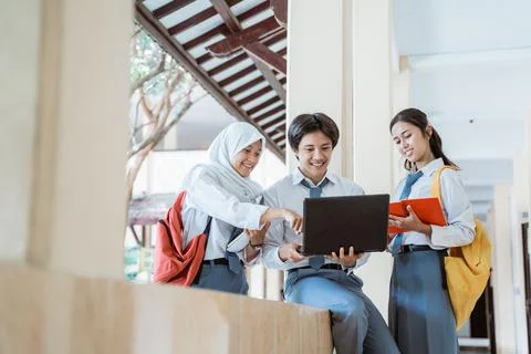 Group of high school students using a laptop computer and carrying books wearing Stock Photos