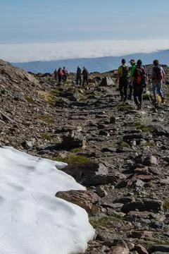 Group of hikers with a patch of snow in the foreground and a sea of low cloud Stock Photos