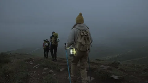 Group of hikers walking along mountain range in misty haze in evening twilight Stock Footage 292307856