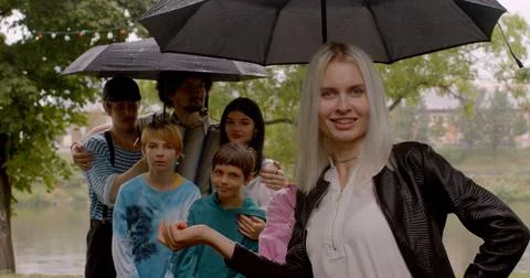 Group joy pose under umbrella rainy weather Blonde woman touches umbrella smiles Stock Photos