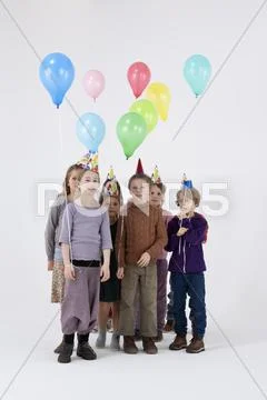 A group of kids wearing party hats and holding balloons Stock Photos