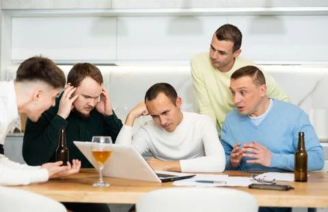 Group of male friends solving problems using laptop and drinking beer Foto stock