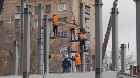 A group of male workers in yellow jackets and hard hats work at a height with Stock Footage 132201246