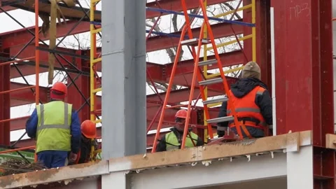A group of male workers in yellow jackets and hard hats work at a height with Stock Footage 132201481