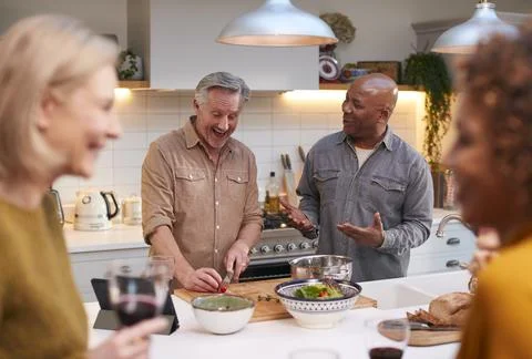 Group Of Mature Friends Meeting At Home Preparing Meal And Drinking Wine Stock Photos