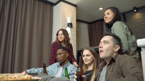 Group of multi-ethnic friends drinking beer and watching TV in the living room Stock Footage 123148042