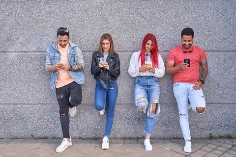Group of multi-ethnic friends using their mobile phones while leaning against a Foto stock