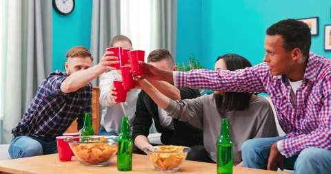 Group of multi-ethnic young joyous friends watching sports match on TV while Stock Footage 152372167