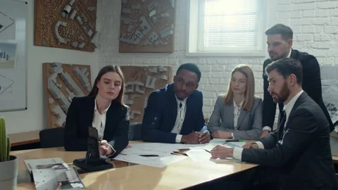 Group of multiethnic colleagues sitting at desk with smartphone and looking at Stock Footage 189031655