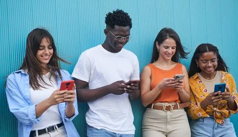 Group of multiethnic young people using mobile phone standing outdoor against Stock Photos