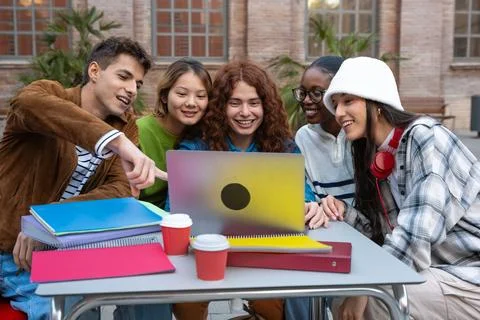 A group of multiracial students with laptops sit near campus to study outdoors. Stock Photos