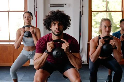 Group of multiracial young adults doing kettlebell squats at the gym Stock Photos