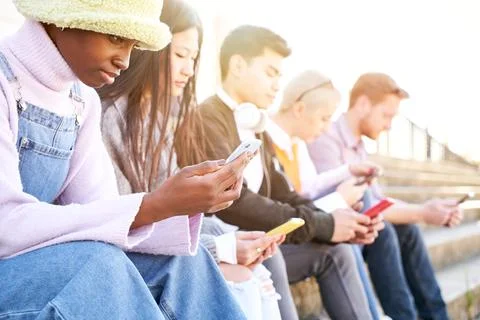 Group of multirracial friends using mobile cell together outdoors watching smart Stock Photos