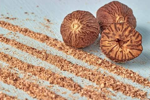 A group of nutmeg nuts and paths with grated nutmeg powder on a light blue .. Stock Photos