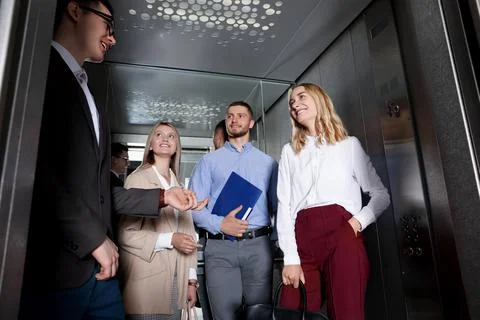 Group of office workers talking in modern elevator Stock Photos